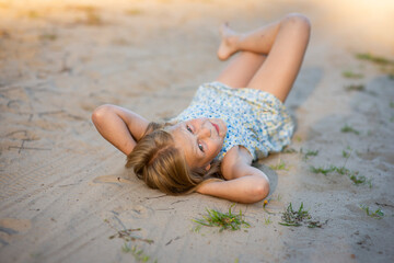 blonde girl in a blue dress lies on the sand, selective focus
