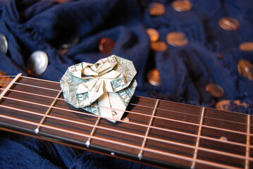 Dollar bill origami heart tucked into guitar strings with coins in background