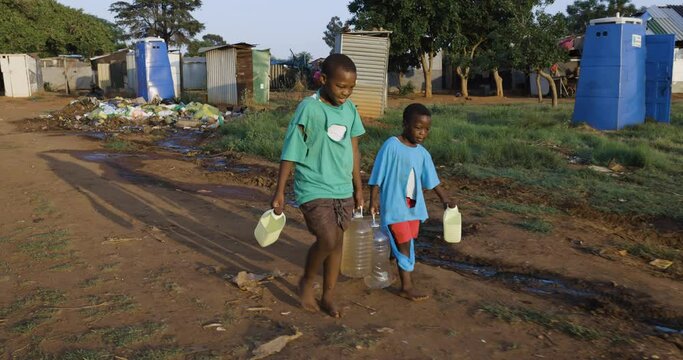 Water crisis. Front close-up view of two young black African boys carrying home dirty unsafe drinking water for domestic use.  Poor living conditions and no access to clean running water