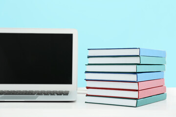Stack of books and laptop on table against color wall