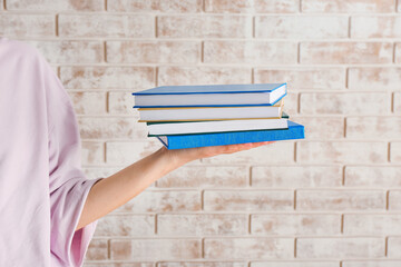 Woman with stack of books against brick wall