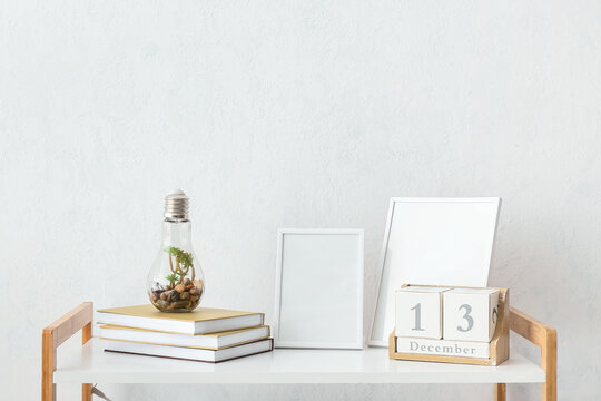 Stack of books, calendar and blank photo frames on table against light wall