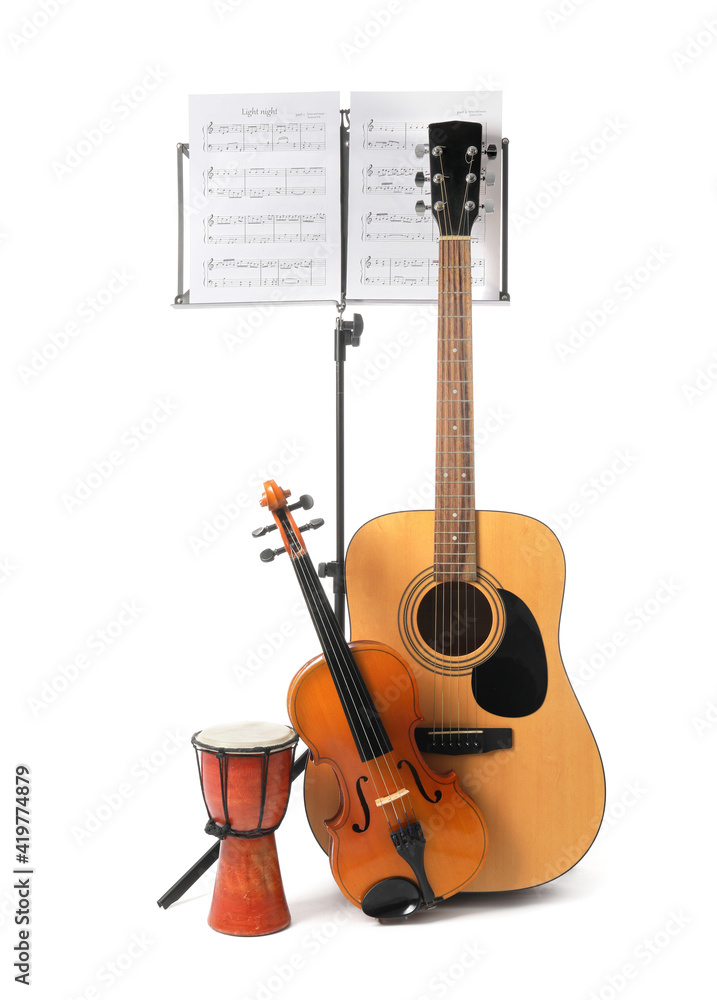 Wall mural note stand with music sheets and different musical instruments on white background