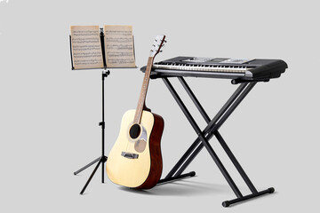Note stand with music sheets, acoustic guitar and synthesizer on light background