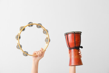 Woman holding tambourine and djembe on light background - obrazy, fototapety, plakaty