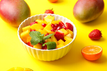 Bowl with tropical fruit salad on color background