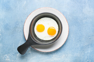 Frying pan with tasty eggs on color background