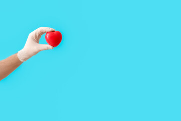 Hand of cardiologist with red heart on color background