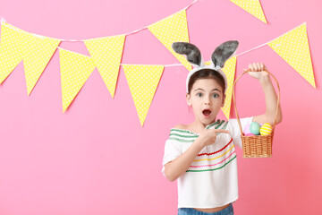 Surprised little girl with bunny ears and Easter eggs on color background