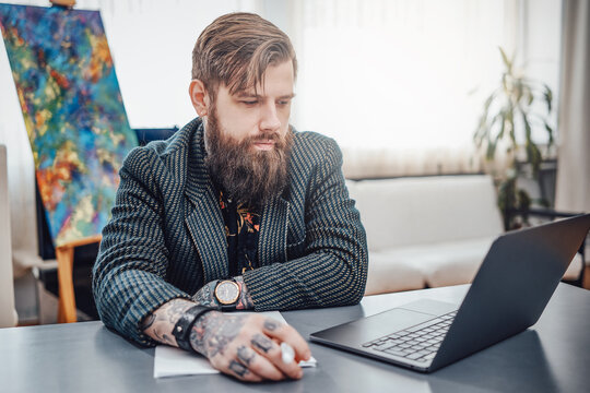Atmospheric portrait of a adult computer programmer with tattoos and wearing stylish clothing. Serious man does his paperwork at table.
