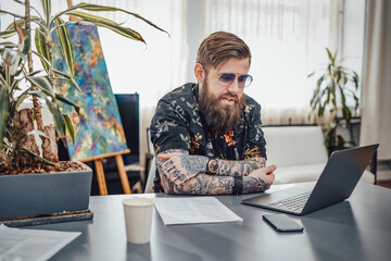 Comfortable workplace for programming and remote working at home. Stylish guy with tattoos and his job on a laptop.