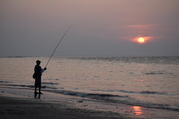A PERSON FISHING NEAR A SEASHORE.
