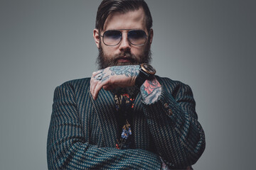 Brutal hipster person with bearded face and fashionable hairstyle poses in gray background with...