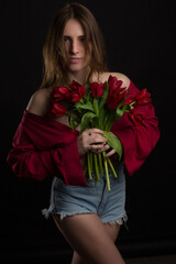 Studio portrait of a young woman on a black background with bouquet of red tulips in her hands