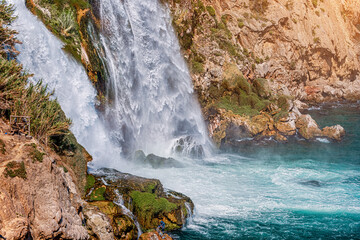 Close-up of a waterfall with splashes and drops falling with a roar from a steep cliff into the sea...