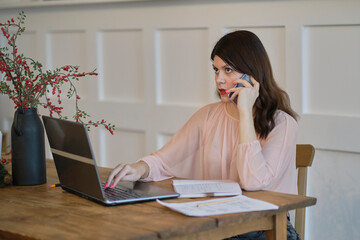 Businesswoman talking on mobile phone working on laptop in cozy home office. free space startup businesswoman online sme telemarketing. Corporate communication.