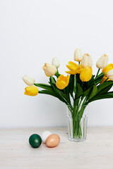 Easter eggs on the table and yellow tulips in a vase Copy Space