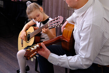 little girl and her father are playing guitar. Learning to play the guitar. Music education and extra-curricular lessons.