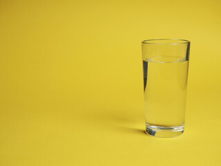 minimalistic concept of water consumption, one glass of water on a yellow background