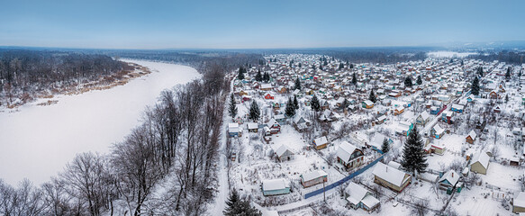 Fototapeta na wymiar Traditional Russian dacha village near river and forest in winter, aerial view