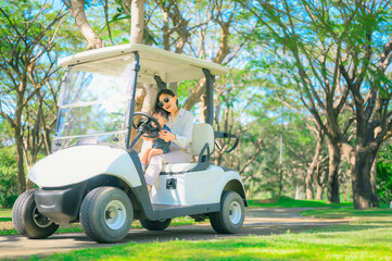 Naklejka premium A woman is sitting at the wheel of a golf car, the son is sitting next to the passenger seat.