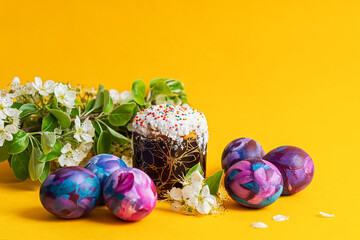 Easter cake, painted eggs and a sprig of a blooming pear on a yellow monochrome background. Happy Easter concept. Home life Easter still life. Individual color of eggs, stylish bright pattern.