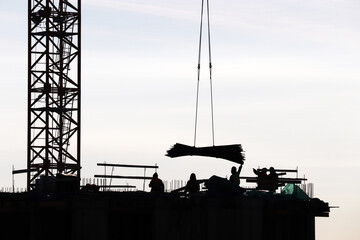 Silhouettes of workers and crane on construction site against the sky. Housing construction, builders working on scaffolding
