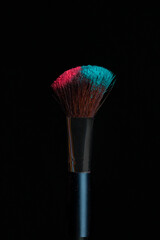 Make-up brush with pink and blue powder isolated on black background