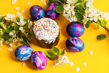 Easter cake, painted eggs and a sprig of a blooming pear on a yellow monochrome background. Happy Easter concept. Home life Easter still life. Individual color of eggs, stylish bright pattern.