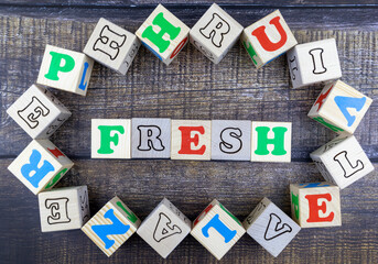 Word - Fresh - in colorful alphabet letters on wooden cubes surrounded by a frame of additional random blocks over a textured textile background. Flat lay, top view