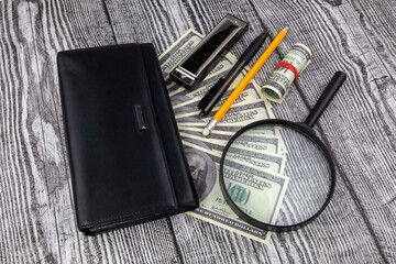 Financial, business success or analysis concept with 100 dollar bills fanned below a purse with magnifying glass, pen and pencil on a decorative wood background in a high angle view