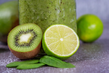 Fototapeta na wymiar Close-up of fresh kiwi and lime fruit halves against a smoothie mug on a gray