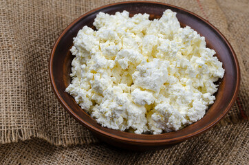 Fresh cottage cheese in a brown clay bowl on a burlap.