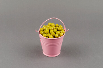 Small pink bucket with canned green peas on a gray background.
