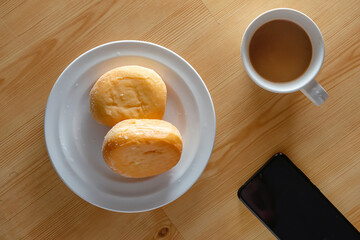 Two doughnuts , cup of white coffee and mobile phone on a light wooden table surface, breakfast concept, top view