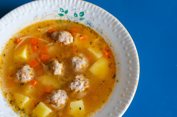 Soup with meatballs in a white ceramic plate on blue.
