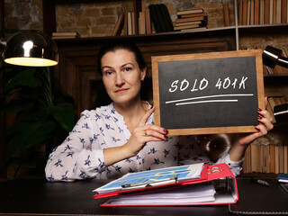 Woman's hand showing chalkboard with phrase SOLO 401K - closeup shot on grey background