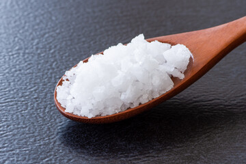 Closeup coarse or rock natural sea salt in wooden spoon isolated on dark background.