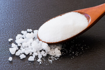 Coarse or rock natural sea salt and salt powder in wooden spoon isolated on dark background.  