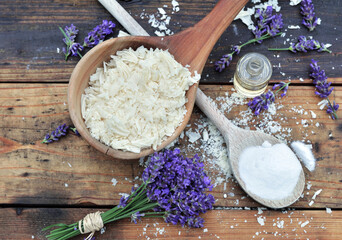 Obraz na płótnie Canvas spoon full of flakes of soap with essential oil and bunch of lavender with bicarbonate on wooden background
