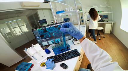 Laboratory doctor holding test tube with blue sample, writing on computer while coworker using...