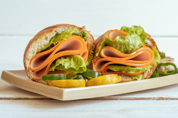 Sandwiches with sausage and fresh lettuce salad on beige plate over wooden background.