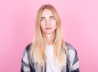 Beautiful young european blonde woman jumping on a pink background in a checkered shirt