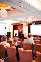 Professional Male Presenter  Speaking In Front of the Group of People in The Hall.