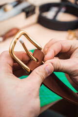 The leather master fastens the gold buckle to the brown belt