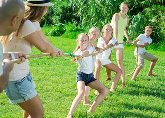 Group of laughing people with little kids having fun together outdoors pulling rope