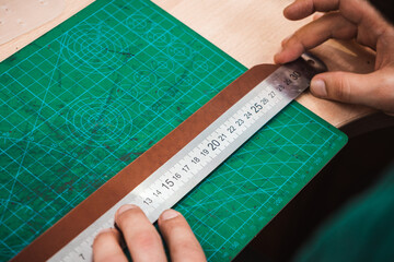 The master measures the leather blank for the belt with a metal line