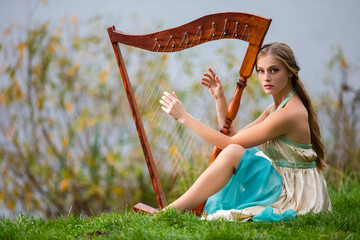 Portrait of Dreaming Sensual Female Harpist in Light Dress Playing Music Outdoor in Park.