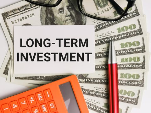 Business and finance concept. Phrase LONG TERM INVESTMENT written on white card with fake money,calculator,a pen and eye glasses.