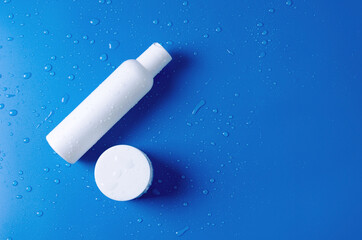 Template concept for the sale of a cosmetic product. White cosmetic bottle with lotion, water, cream and jar of face care cream on blue background with water drops, copy space and flat lay
